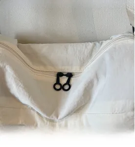 Close-up of smooth dual black zippers with metal ring pulls on a white nylon crossbody bag