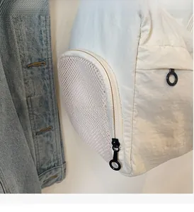 Detail of smooth zipper with round pull and mesh side pocket on beige travel bag