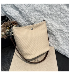 Détail de la texture tressée du sac seau crème avec bandoulière en cuir marron