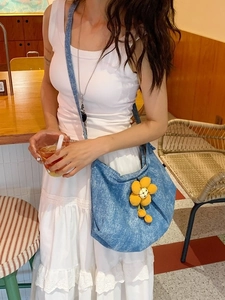 Sac à bandoulière en denim avec fleur jaune porté par un mannequin dans un café chic