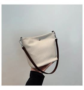 Détail d'un sac seau tressé crème avec bandoulière en cuir marron et fermoir argenté