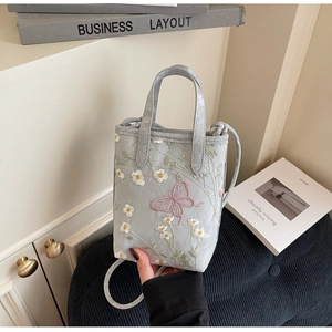 Détail du sac cabas gris avec broderie délicate de fleurs blanches et papillon rose