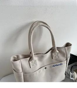 Close-up of beige canvas tote bag showing AlManQi blue embroidery and side pocket