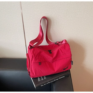 Detail of red nylon crossbody bag with BNT logo and adjustable strap on dark leather surface