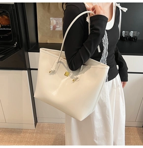 Detailed view of cream white tote bag with gold knot hardware and square logo plate