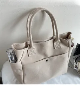 Detail of canvas tote bag featuring side pockets and a front pocket with a black metal snap