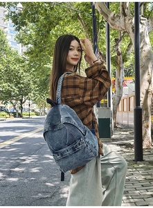 Detailed side view of a blue washed denim backpack with adjustable straps in sunlight