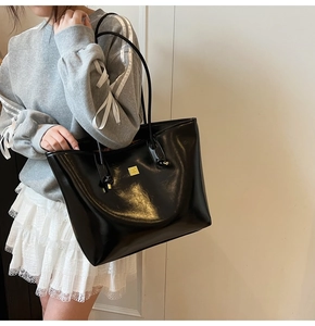 Close-up of a black glossy tote bag with a gold square logo and slim shoulder straps