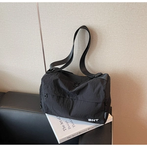 Detail of a lightweight black nylon crossbody bag featuring white BNT lettering on front