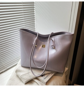 Detail of lavender glossy tote bag featuring a gold logo plate and slim knot handles