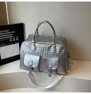Detail of silver woven texture travel bag featuring dual flap pockets and top handles