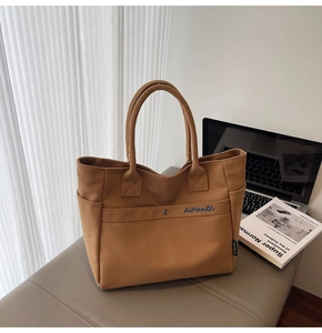 Detail of a brown canvas tote bag with blue embroidery and thick handles on a bench