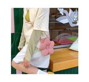 Dettaglio di una borsa a tracolla a quadretti rossi a forma di fiore indossata dal modello
