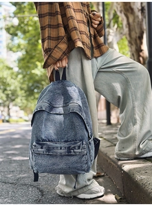 Outdoor street view of a blue denim backpack with zipper pockets held by a model