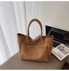 Detail of a dark brown canvas tote bag with blue embroidery on a grey leather bench