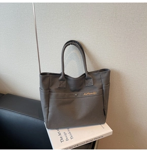 Detail of grey canvas tote bag with snap button front pocket and gold logo lettering