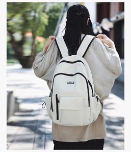 Rear view of a minimalist white canvas backpack with black zipper details and side pockets