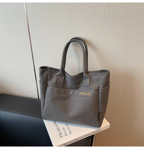 Detail of dark grey canvas tote bag featuring metal buckles and side pockets on books