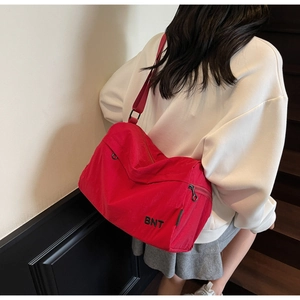 Detail of red nylon shoulder bag featuring black BNT embroidery and wide fabric strap