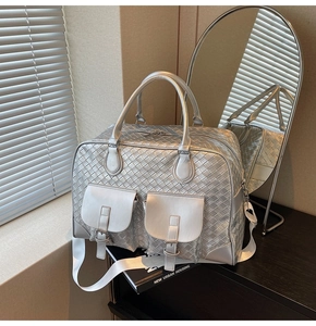 Detailed view of silver woven travel bag featuring dual front buckle pockets and cross strap
