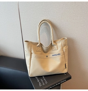 Detailed macro view showing the sturdy canvas texture and dark blue AiManQi embroidery on tote bag