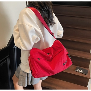 Detail of red nylon crossbody bag with BNT logo on a wooden staircase background