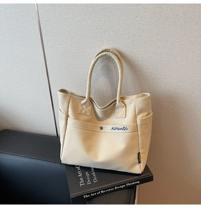 Detail of beige canvas tote bag showing side pockets and metal snap closure