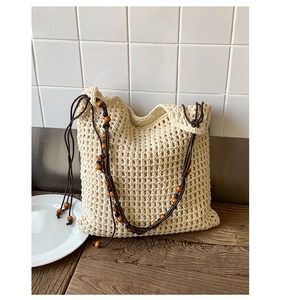 Close-up of beige crochet knit beach tote bag featuring decorative wooden beads on the strap