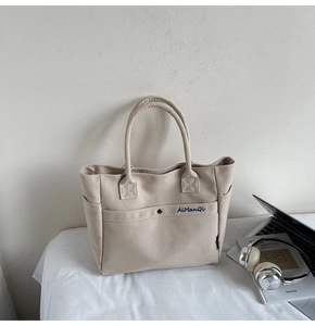 Close-up of beige canvas tote bag with metal snap pocket and minimalist embroidery