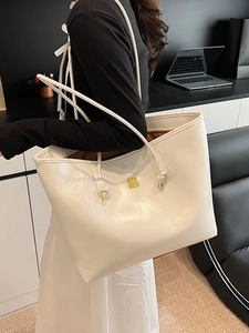 Large white faux leather tote bag with gold logo on shoulder of model in a modern room