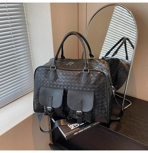 Detail of black woven leather travel bag with dual front buckle pockets and sturdy handles