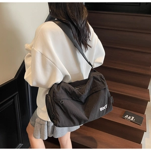 Close-up of black nylon crossbody bag with BNT logo on a wooden staircase background