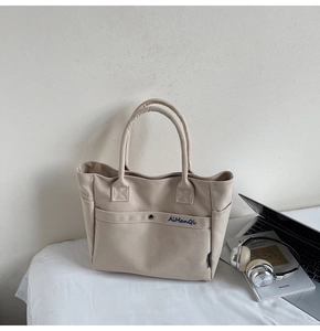 Detail of beige canvas tote bag with blue AiManQi embroidery and laptop setup