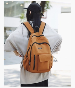 Outdoor view of a mustard yellow canvas backpack featuring an HYFC logo patch