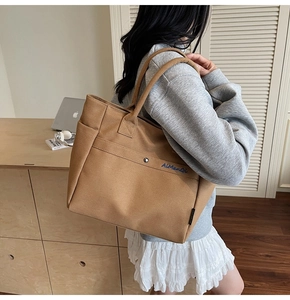 Brown canvas tote bag with front pocket and blue logo embroidery on casual model