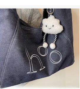 Detail of dark blue denim tote bag with white embroidery and plush cloud keychain