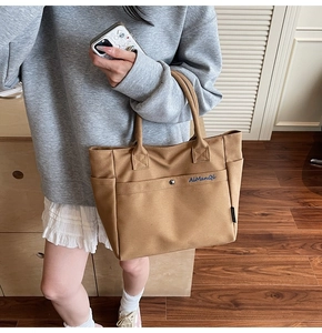 Detail of tan canvas tote bag with metal snap pocket and reinforced handles