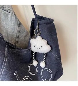 Detail of a white plush cloud charm with smiley embroidery on a denim tote bag