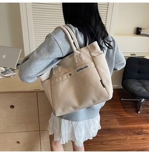 Detail of beige canvas tote bag with blue embroidery and functional side pocket for daily use