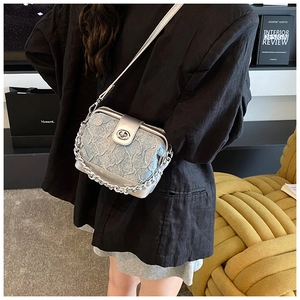 Detail of light blue denim crossbody bag with silver leather trim and oval metal turn-lock
