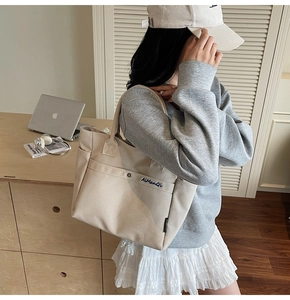Close-up of beige canvas tote bag with snap pocket and branding label on the side