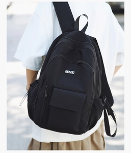 Outdoor view of a black minimalist backpack with MYJC logo and wide shoulder straps
