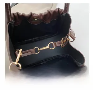Detail of a brown leather handbag showing golden metal chain hooks and magnetic closure