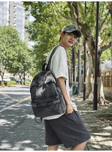 Side view of a vintage charcoal washed denim backpack worn on a sunlit urban street