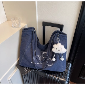 Detail of blue denim tote bag with white hoo embroidery and plush cloud charm