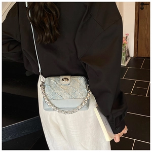 Detail of light blue quilted denim handbag with silver chain strap and metal clasp