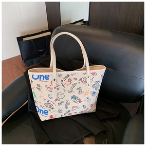 Détail d'un sac cabas blanc avec des motifs graffiti colorés sur une chaise en cuir noir