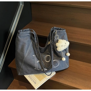 Detail of dark blue denim tote bag featuring white ho art text and cloud plush charm