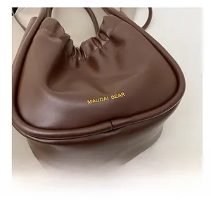 Detail shot of a dark brown pleated handbag featuring a gold metallic logo and soft leather texture