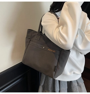 Close-up of brown canvas tote bag featuring front pocket with metal snap and logo embroidery